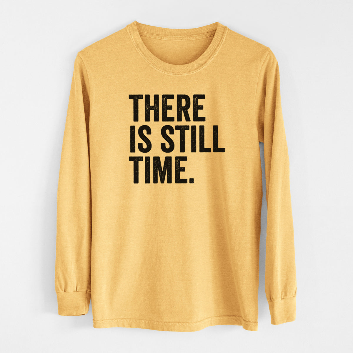 Golden wheat yellow Comfort Colors long sleeve shirt laid flat, printed with bold black words reading There Is Still Time.