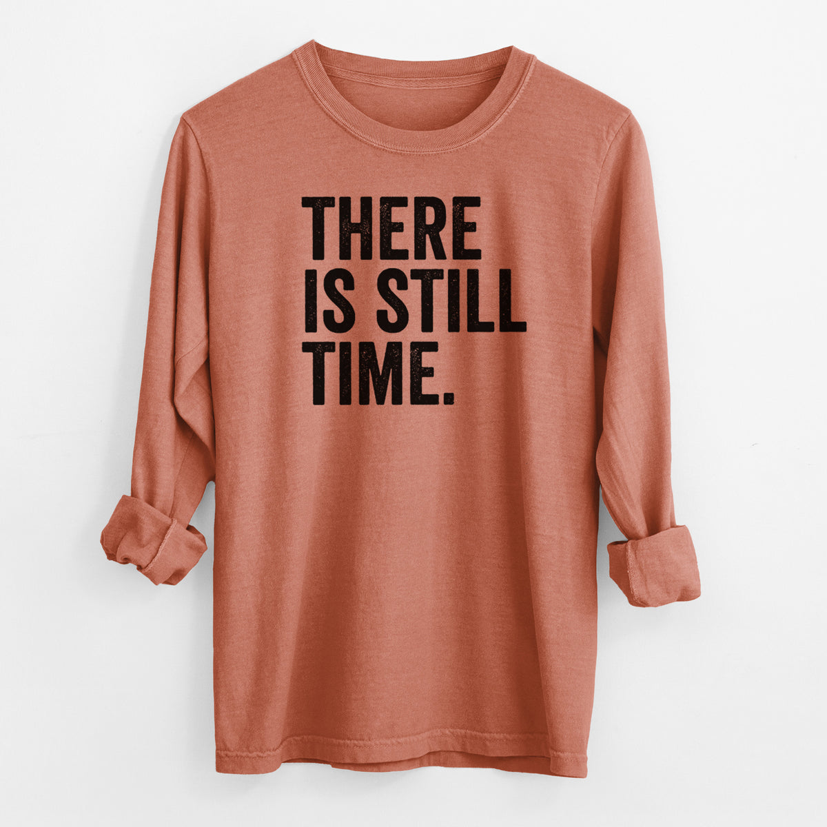 Yam burnt orange Comfort Colors long sleeve shirt laid flat with the cuffs rolled, printed with bold black words reading There Is Still Time.