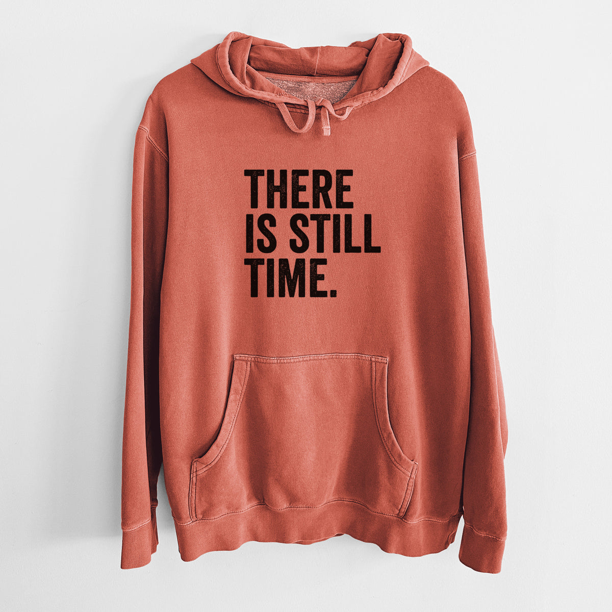 Amber orange pigment dyed hoodie laid flat, printed with bold black words reading There Is Still Time.