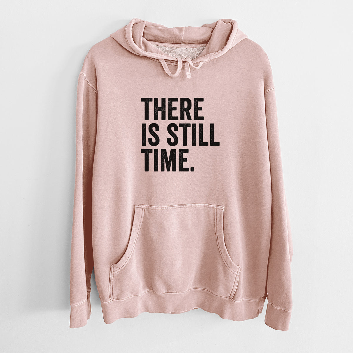 Dusty pink pigment dyed hoodie laid flat, printed with bold black words reading There Is Still Time.