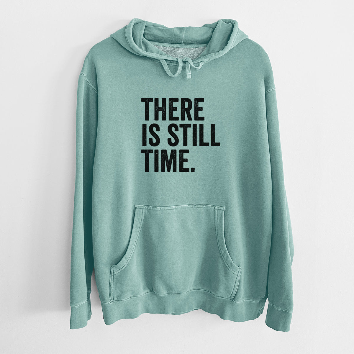 Mint green pigment dyed hoodie laid flat, printed with bold black words reading There Is Still Time.