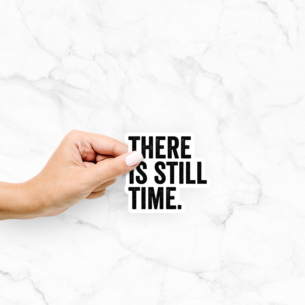 Hand holding a 4 inch vinyl decal of bold black words reading There Is Still Time.