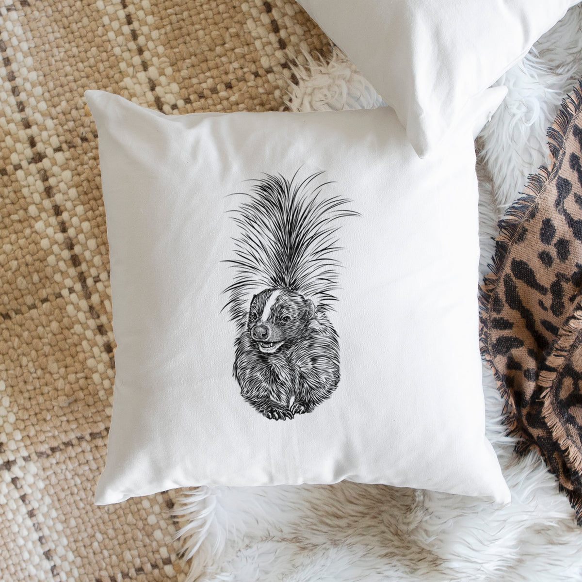 White pillow cover printed with a detailed black ink illustration of a striped skunk with its tail raised, on a woven chair.