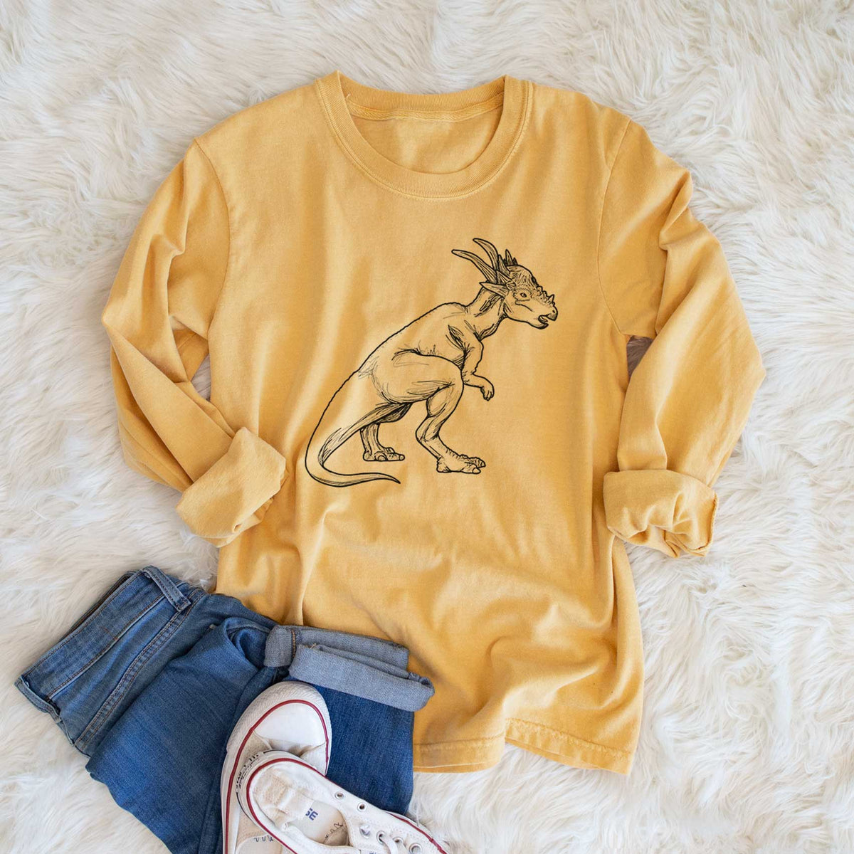 Golden wheat yellow Comfort Colors long sleeve shirt printed with a black ink illustration of a Stygimoloch dinosaur with a spiky domed head, shown in a lifestyle photo.