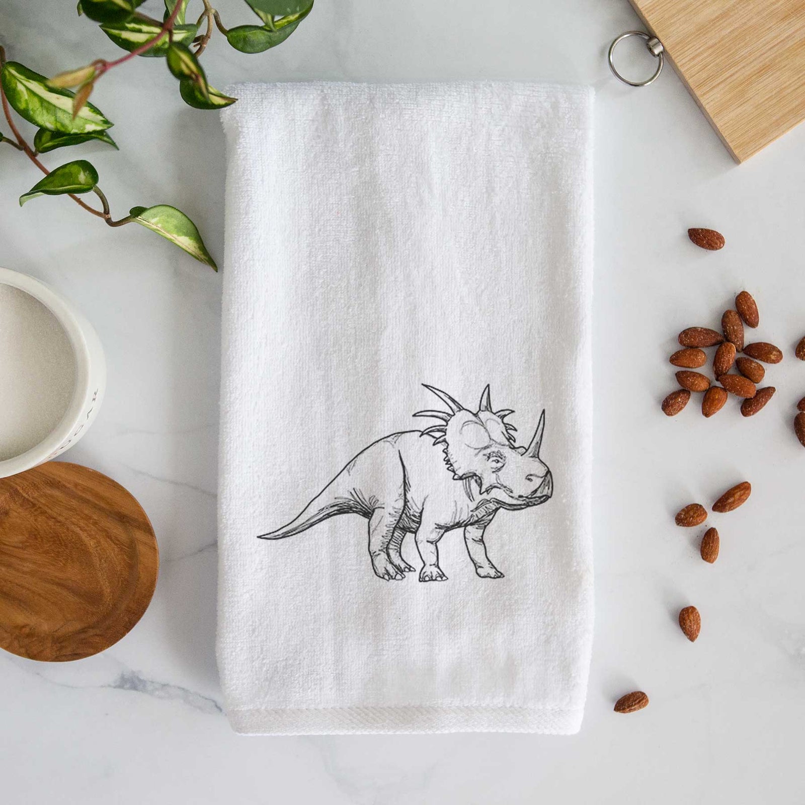 White hand towel printed with a black ink illustration of a Styracosaurus with its spiked frill.
