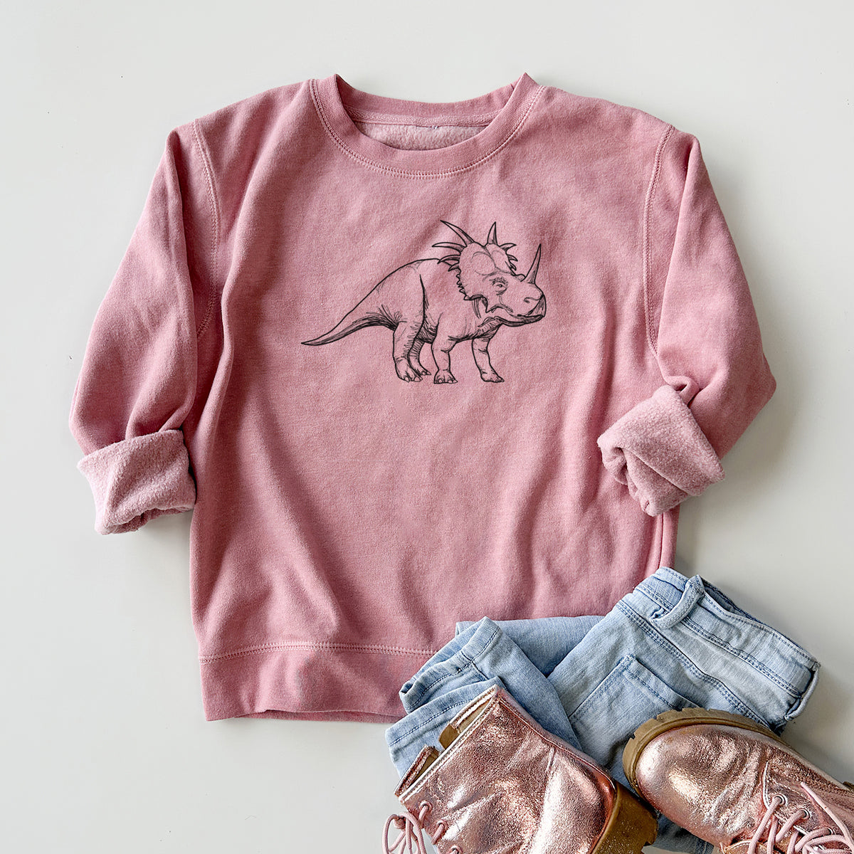 Youth crewneck sweatshirt printed with a black ink illustration of a Styracosaurus with its spiked frill, styled flat with jeans and boots.