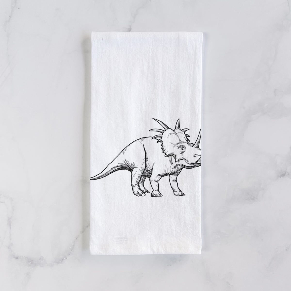 White cotton tea towel laid flat on marble, printed with a black ink illustration of a Styracosaurus with its spiked frill.