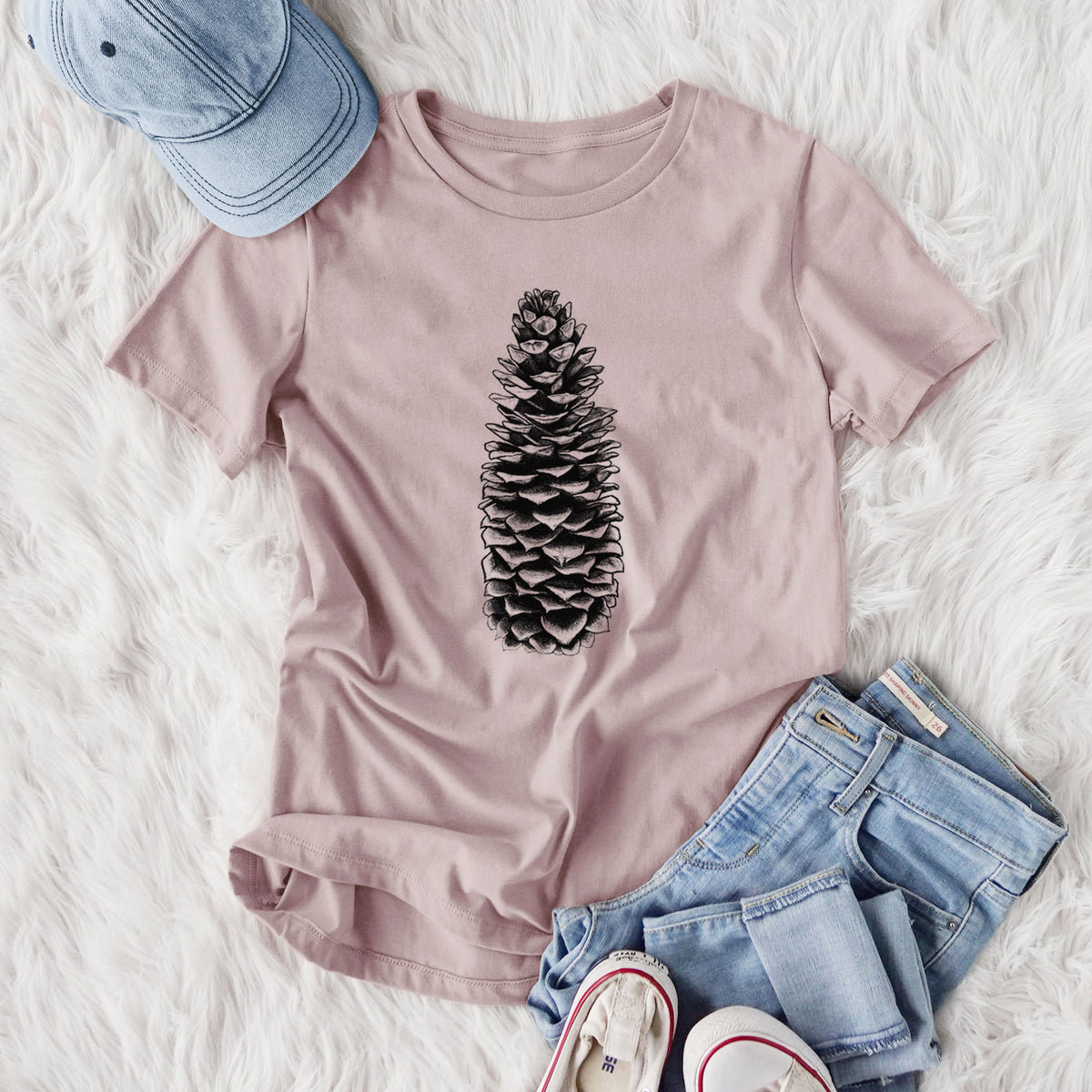 Women's relaxed fit cotton t-shirt printed with a detailed black ink illustration of a long sugar pine cone, styled flat on a white faux fur rug with jeans.