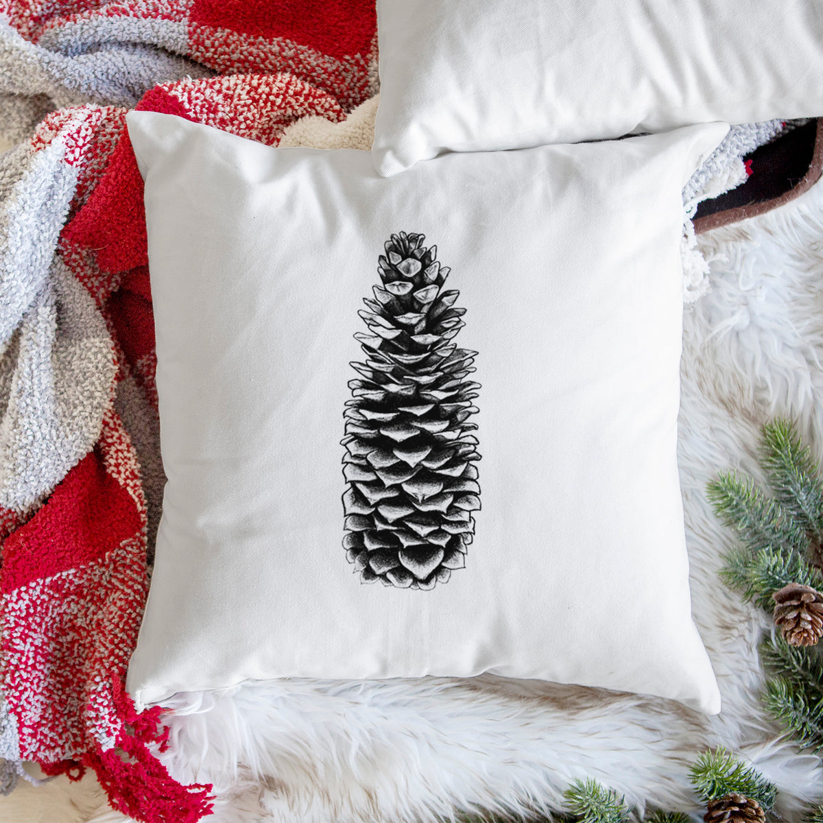 White pillow cover printed with a detailed black ink illustration of a long sugar pine cone, on a woven chair.
