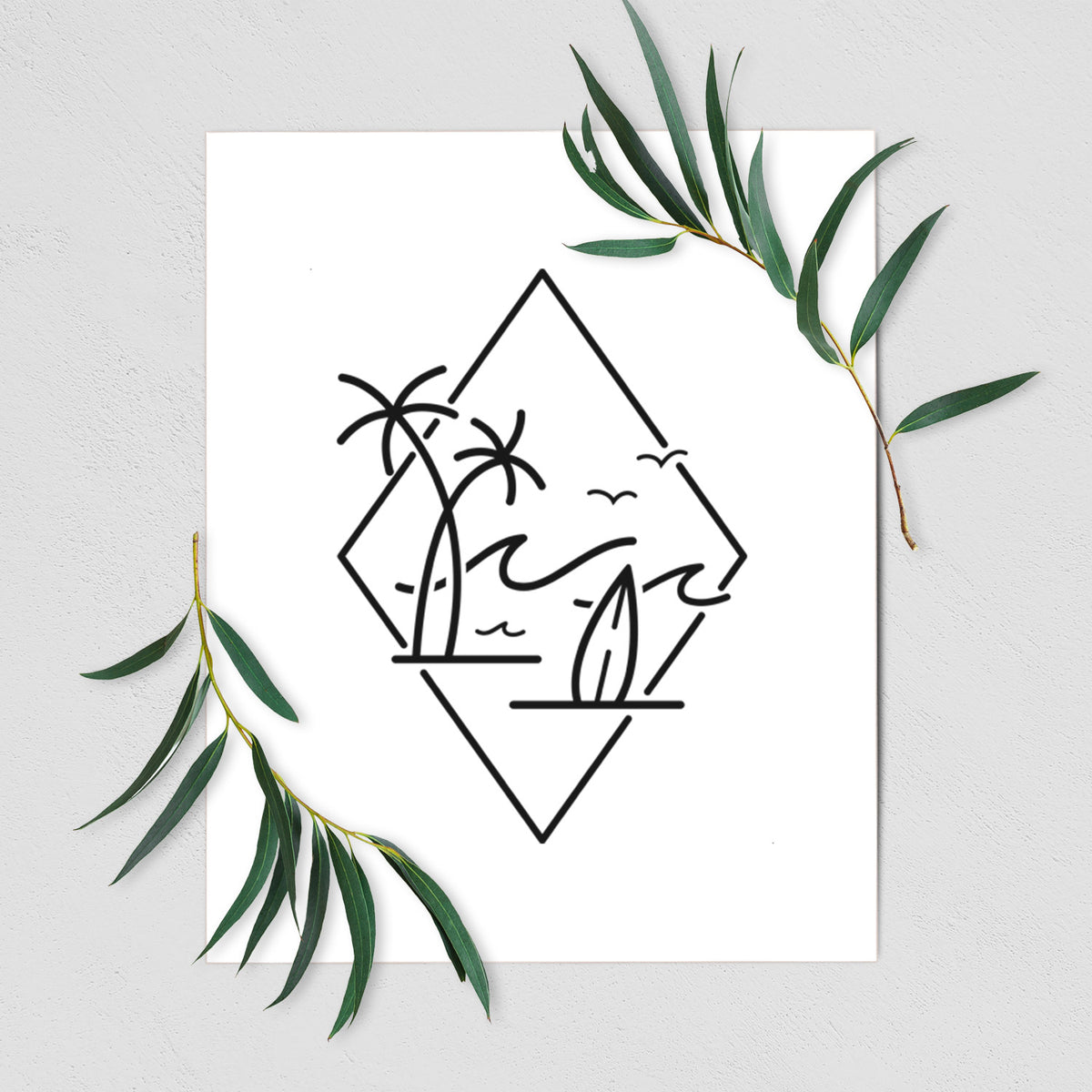 Art print of black line art of palm trees, ocean waves, birds and a surfboard inside a diamond outline, shown with eucalyptus leaves.