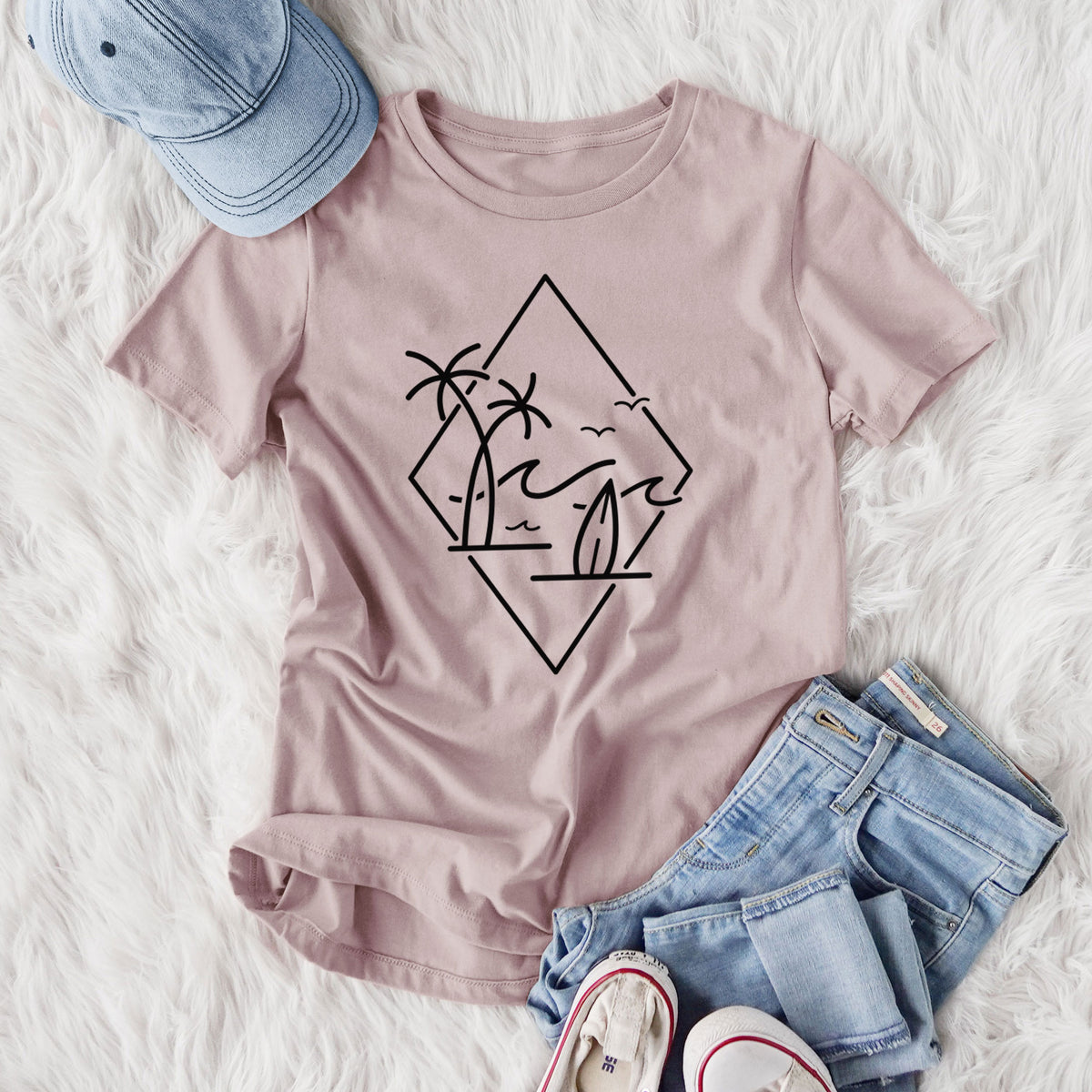 Women's relaxed fit cotton t-shirt printed with black line art of palm trees, ocean waves, birds and a surfboard inside a diamond outline, styled flat on a white faux fur rug with jeans.
