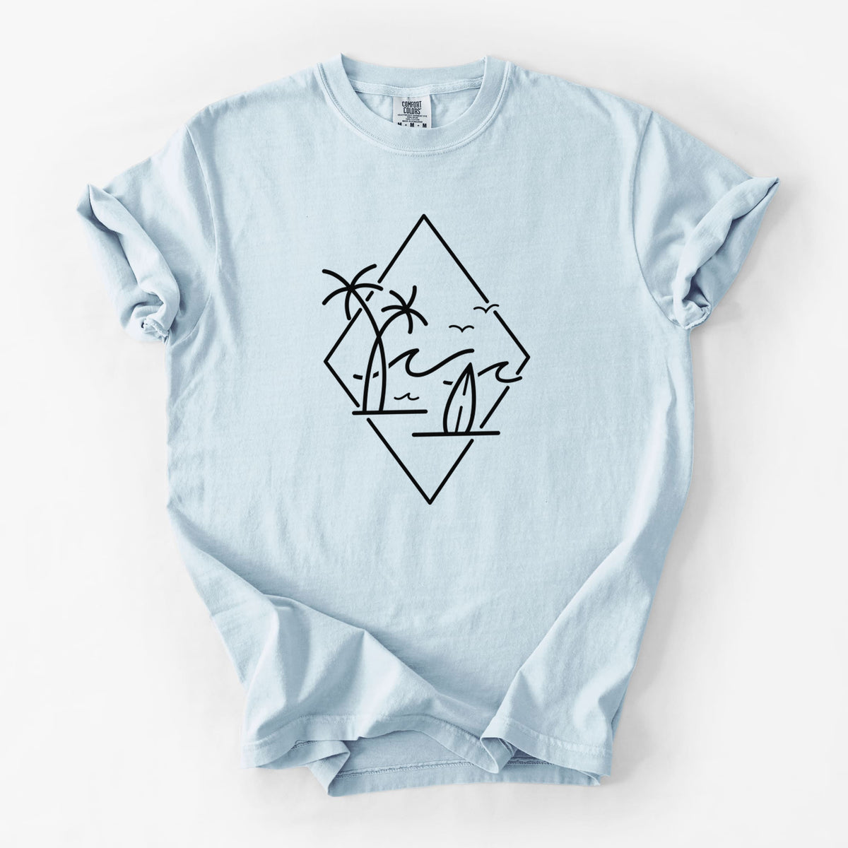 Chambray blue Comfort Colors t-shirt laid flat, printed with black line art of palm trees, ocean waves, birds and a surfboard inside a diamond outline.