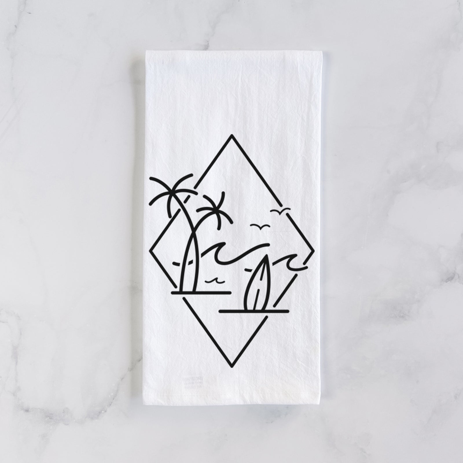 White cotton tea towel printed with black line art of palm trees, ocean waves, birds and a surfboard inside a diamond outline, on a marble counter beside a round wooden cutting board and greenery.