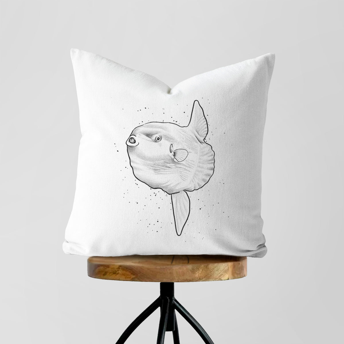 White pillow cover printed with a black ink illustration of an ocean sunfish swimming, on a wooden stool.