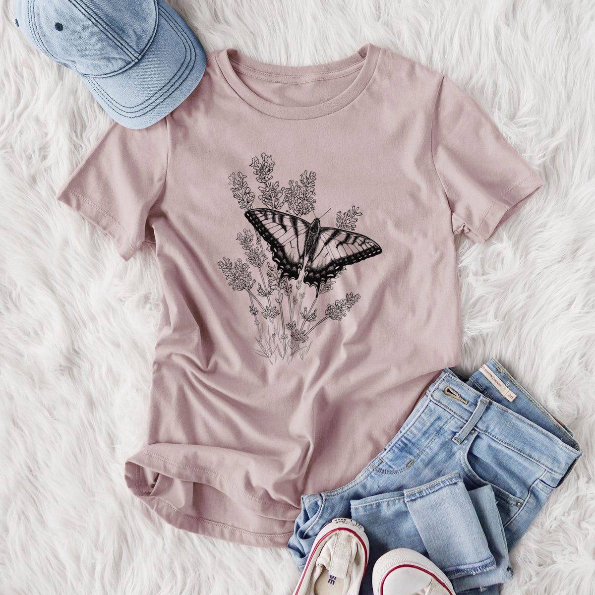 Women's relaxed fit cotton t-shirt printed with a black ink illustration of a swallowtail butterfly resting on lavender, styled flat on a white faux fur rug with jeans.