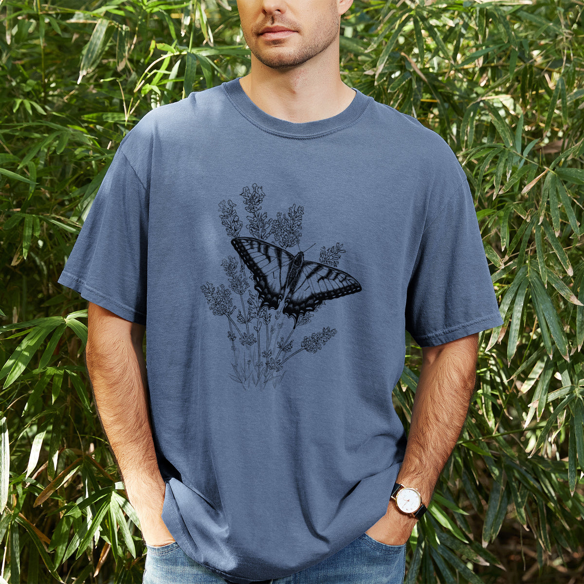 Man wearing a Comfort Colors t-shirt printed with a black ink illustration of a swallowtail butterfly resting on lavender, outdoors.
