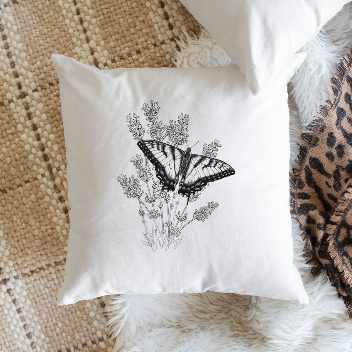 White pillow cover printed with a black ink illustration of a swallowtail butterfly resting on lavender, on a woven chair.