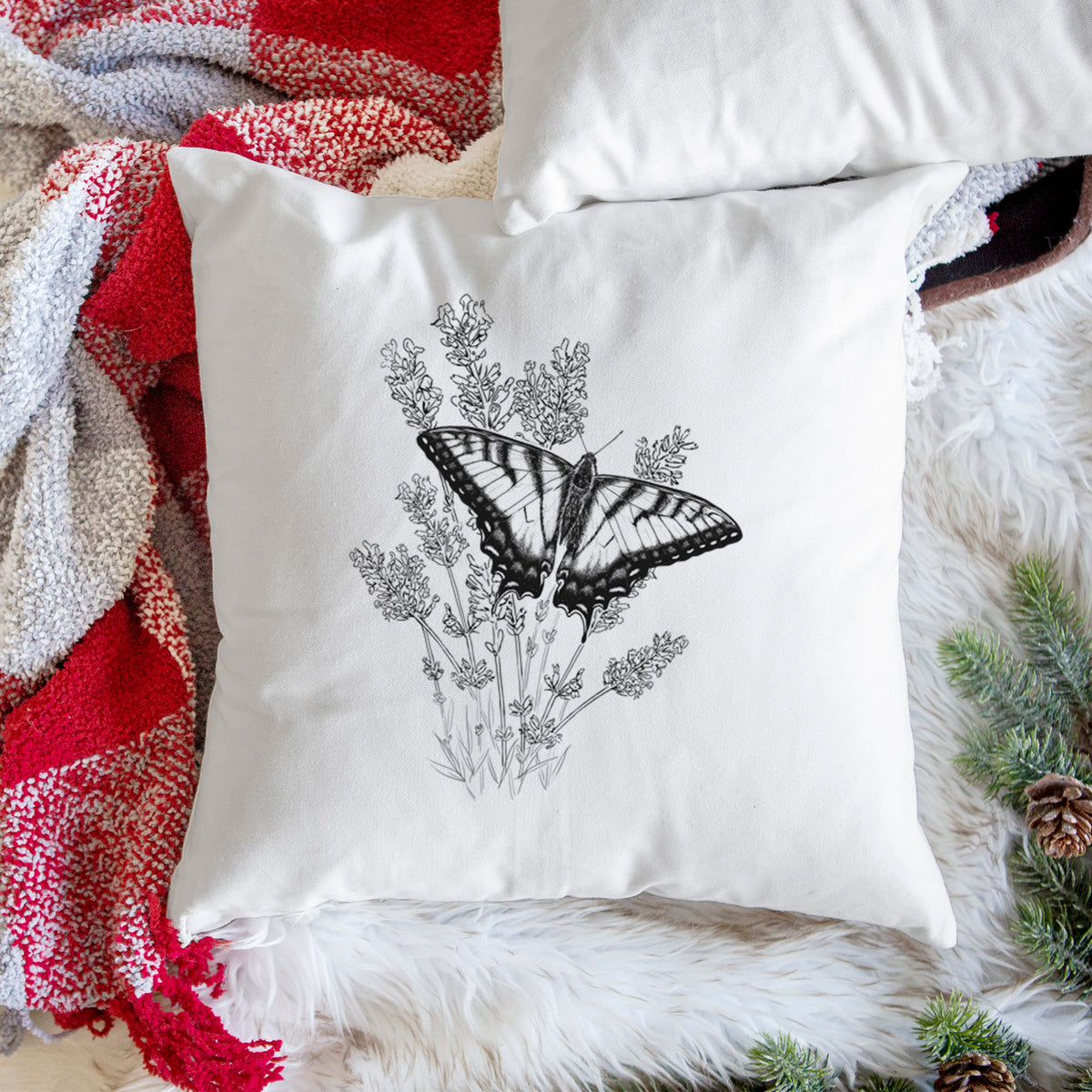White pillow cover printed with a black ink illustration of a swallowtail butterfly resting on lavender, on a woven chair.