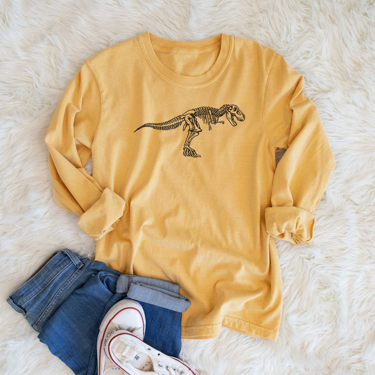 Golden wheat yellow Comfort Colors long sleeve shirt printed with a black ink illustration of a Tyrannosaurus rex skeleton, shown in a lifestyle photo.