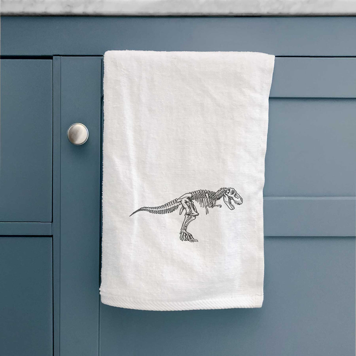 White hand towel printed with a black ink illustration of a Tyrannosaurus rex skeleton.