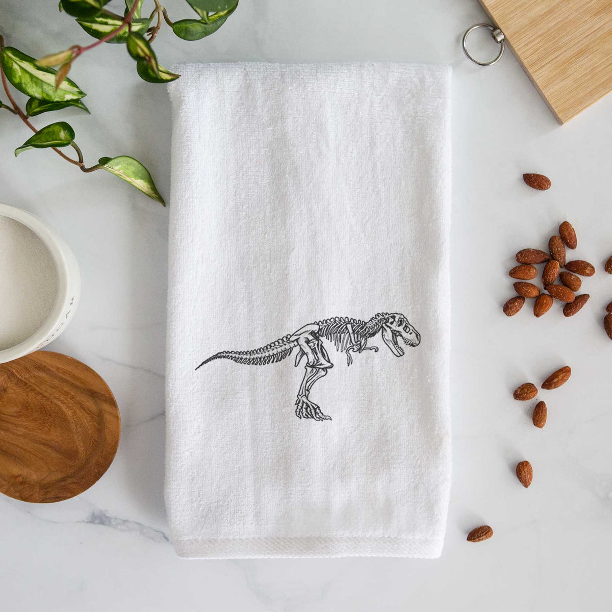 White hand towel printed with a black ink illustration of a Tyrannosaurus rex skeleton.
