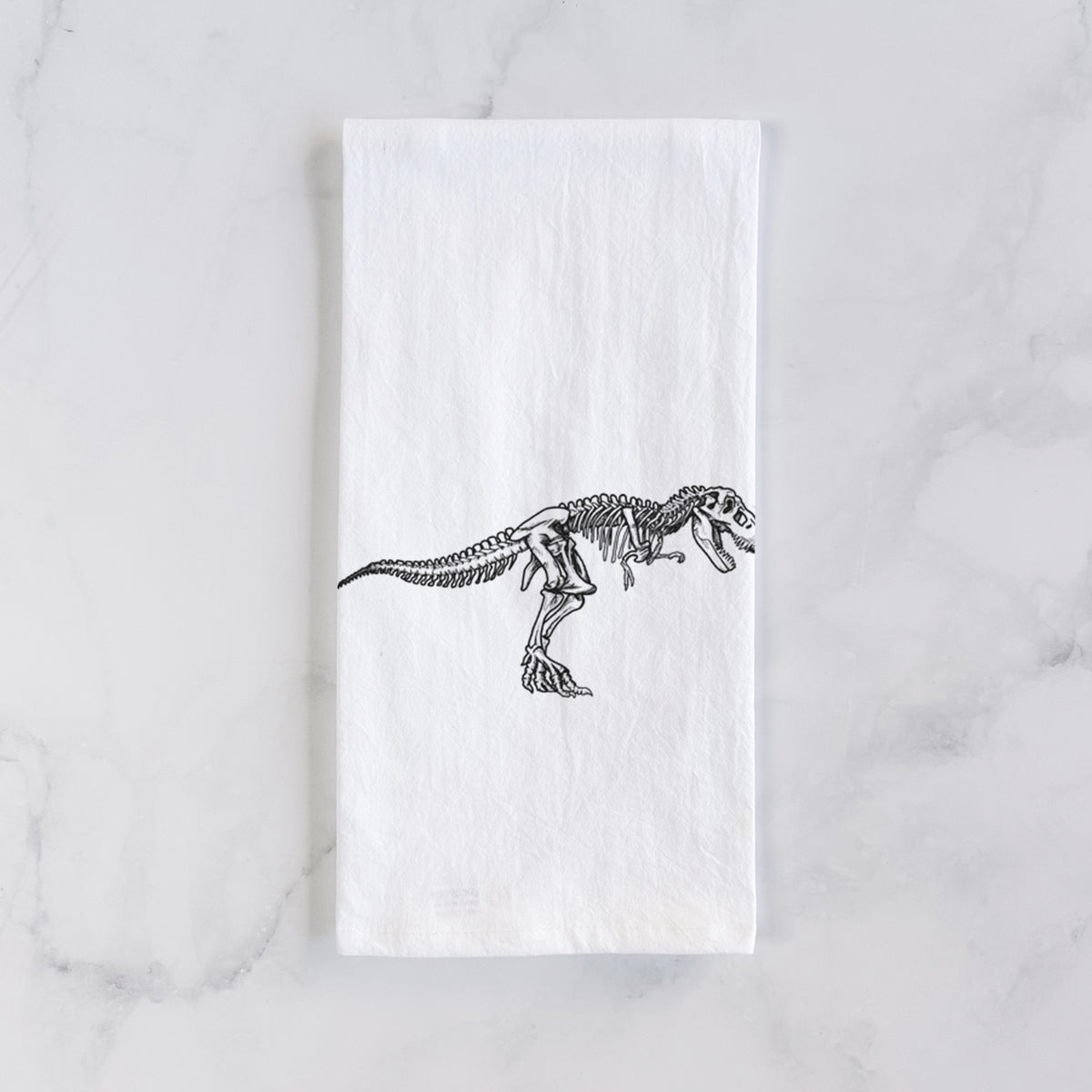 White cotton tea towel laid flat on marble, printed with a black ink illustration of a Tyrannosaurus rex skeleton.