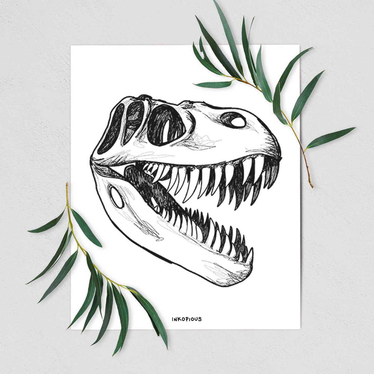 Art print of a black ink illustration of a Tyrannosaurus rex skull with sharp teeth, shown with eucalyptus leaves.