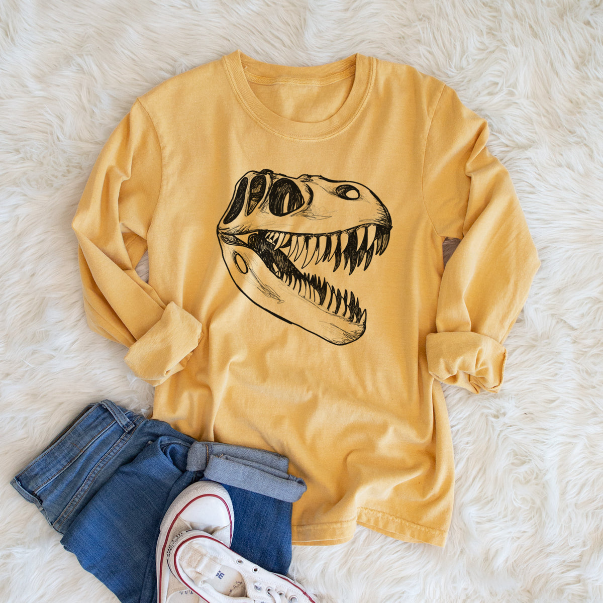 Golden wheat yellow Comfort Colors long sleeve shirt printed with a black ink illustration of a Tyrannosaurus rex skull with sharp teeth, shown in a lifestyle photo.
