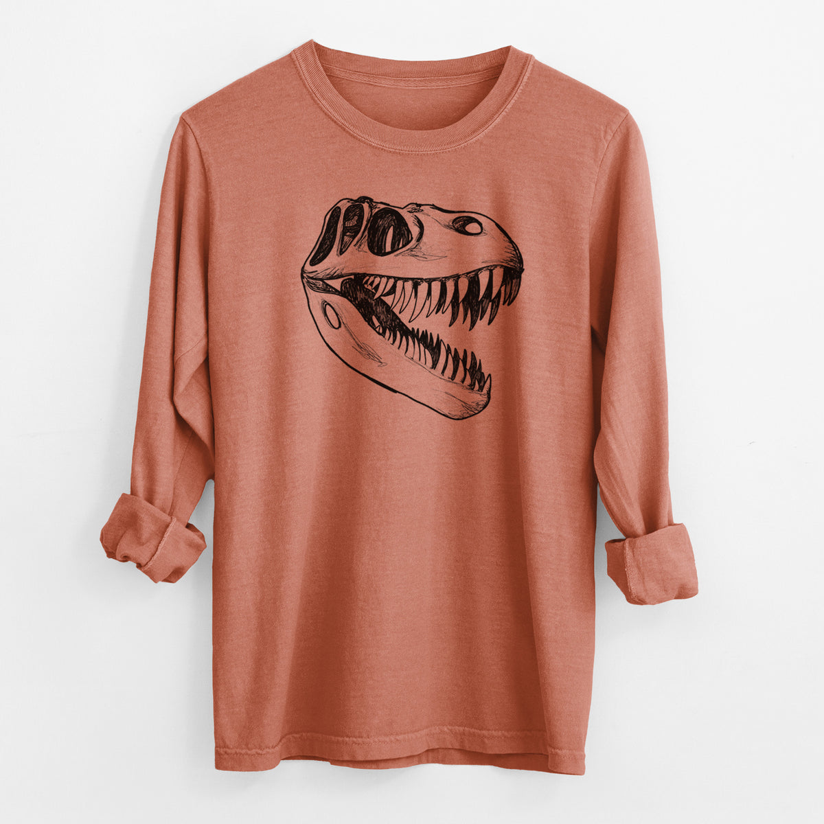 Yam burnt orange Comfort Colors long sleeve shirt laid flat with the cuffs rolled, printed with a black ink illustration of a Tyrannosaurus rex skull with sharp teeth.
