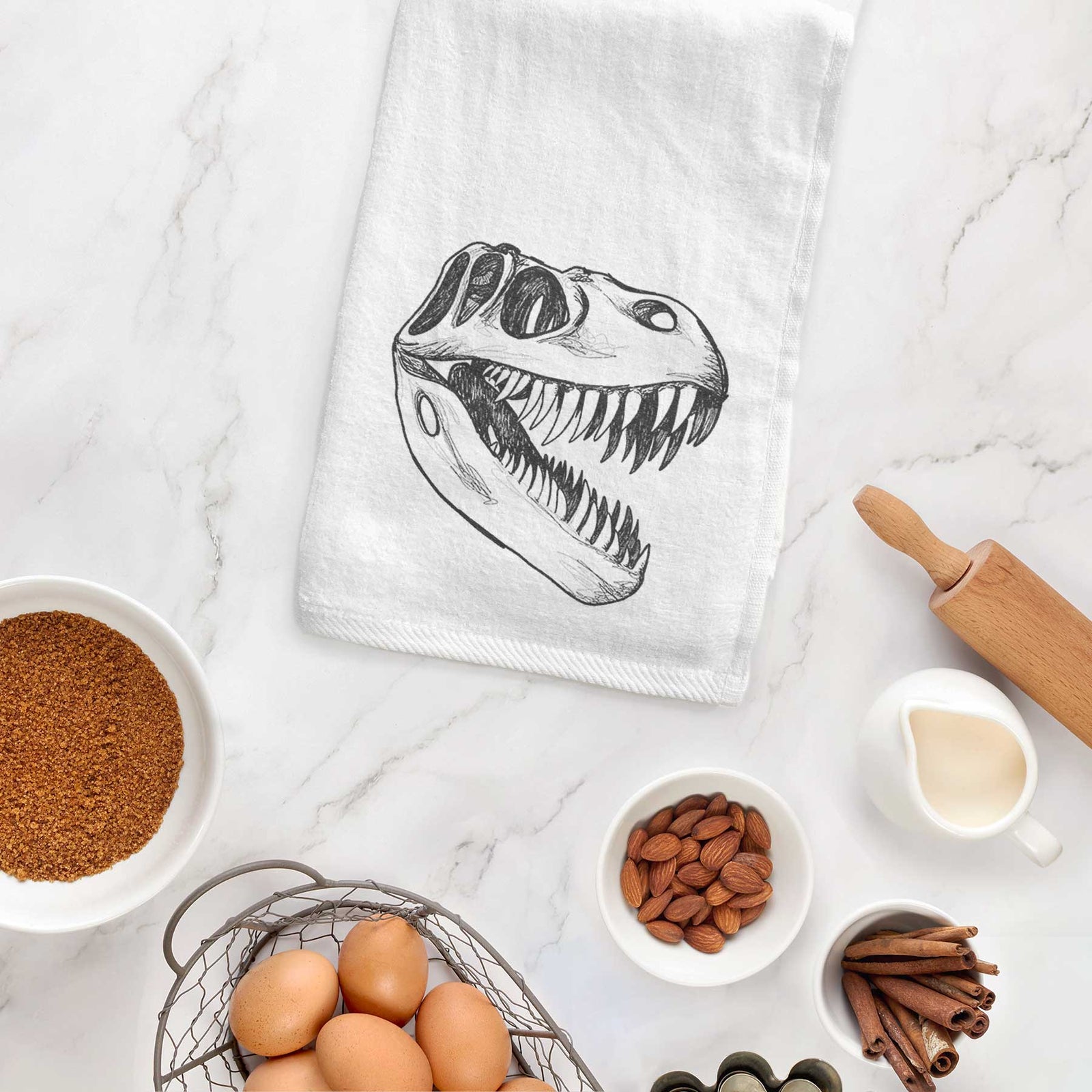 White hand towel printed with a black ink illustration of a Tyrannosaurus rex skull with sharp teeth.