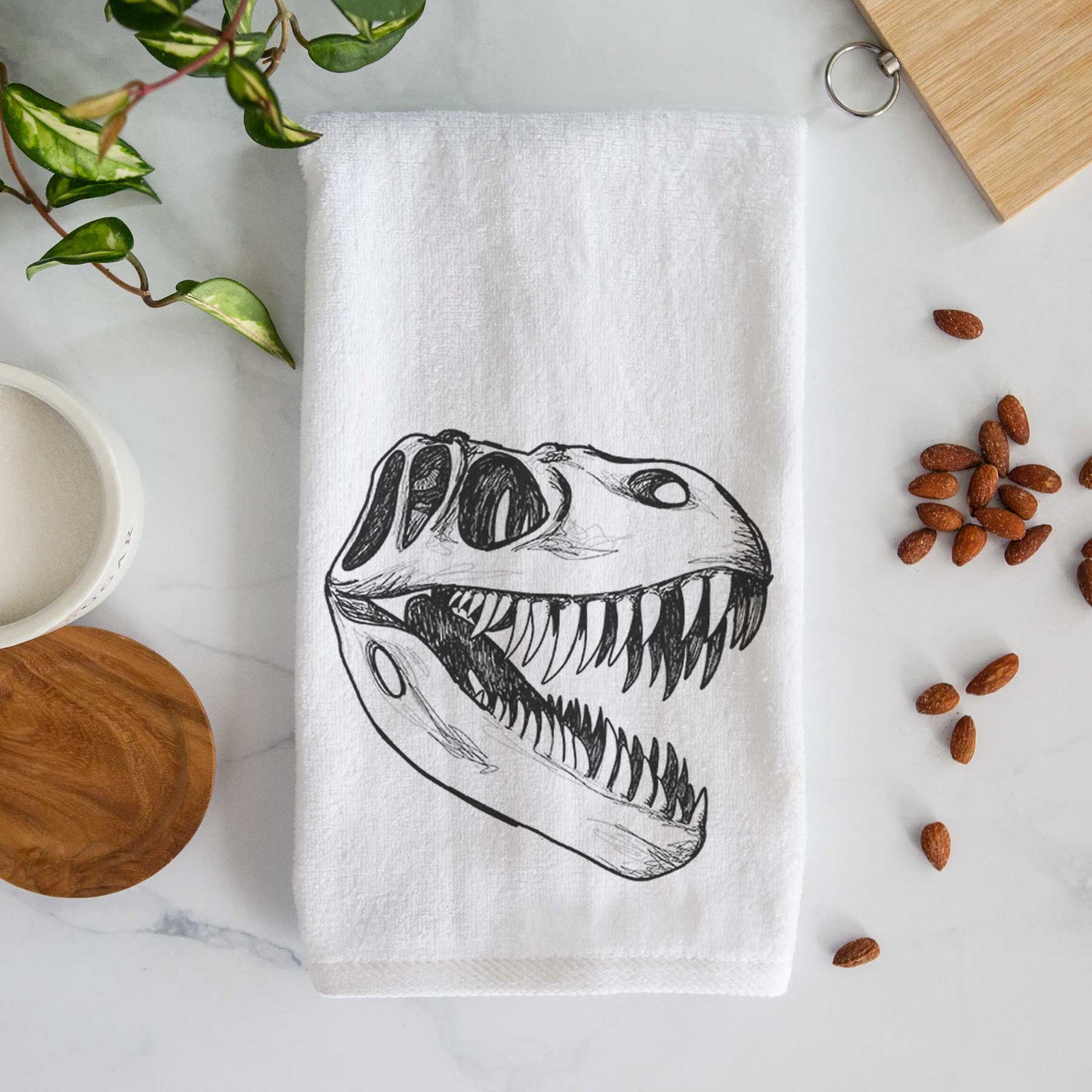 White hand towel printed with a black ink illustration of a Tyrannosaurus rex skull with sharp teeth.