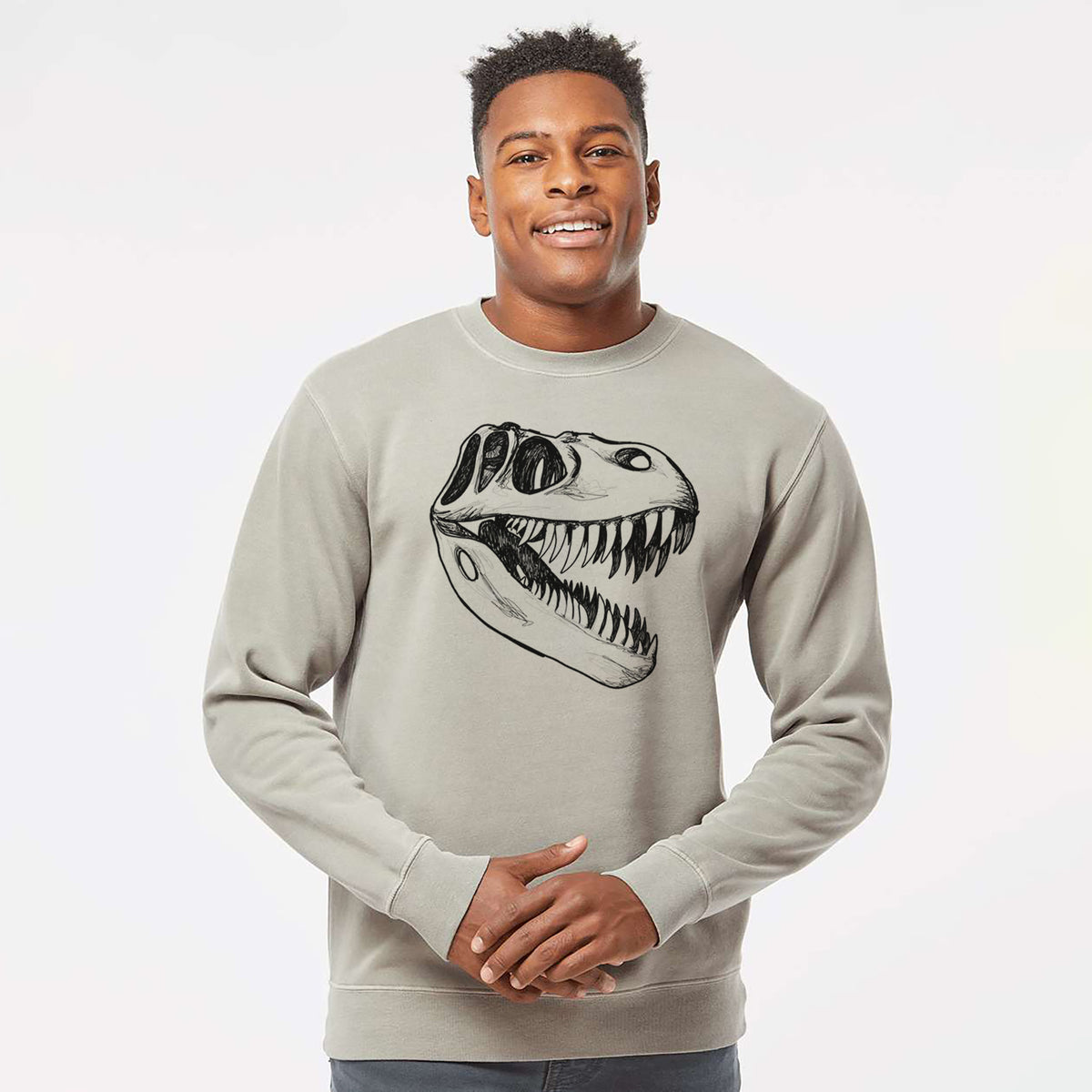 Model wearing a cement grey pigment dyed crewneck sweatshirt printed with a black ink illustration of a Tyrannosaurus rex skull with sharp teeth.