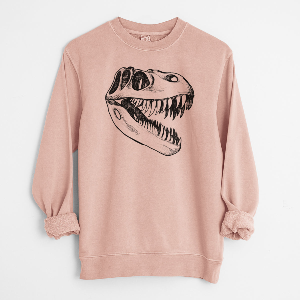 Dusty pink pigment dyed crewneck sweatshirt laid flat with the sleeves rolled, printed with a black ink illustration of a Tyrannosaurus rex skull with sharp teeth.