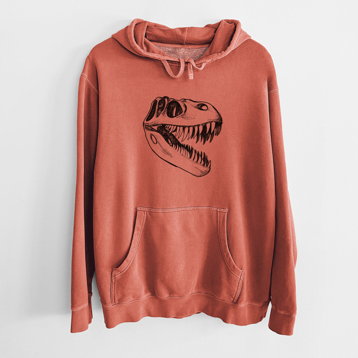Amber orange pigment dyed hoodie laid flat, printed with a black ink illustration of a Tyrannosaurus rex skull with sharp teeth.