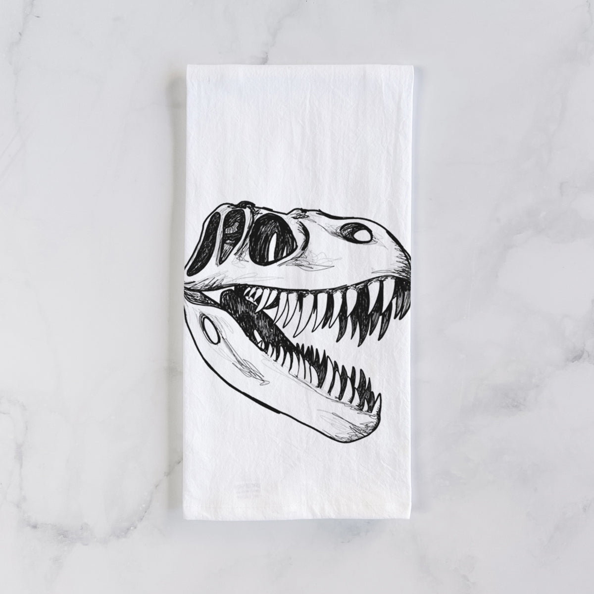 White cotton tea towel laid flat on marble, printed with a black ink illustration of a Tyrannosaurus rex skull with sharp teeth.