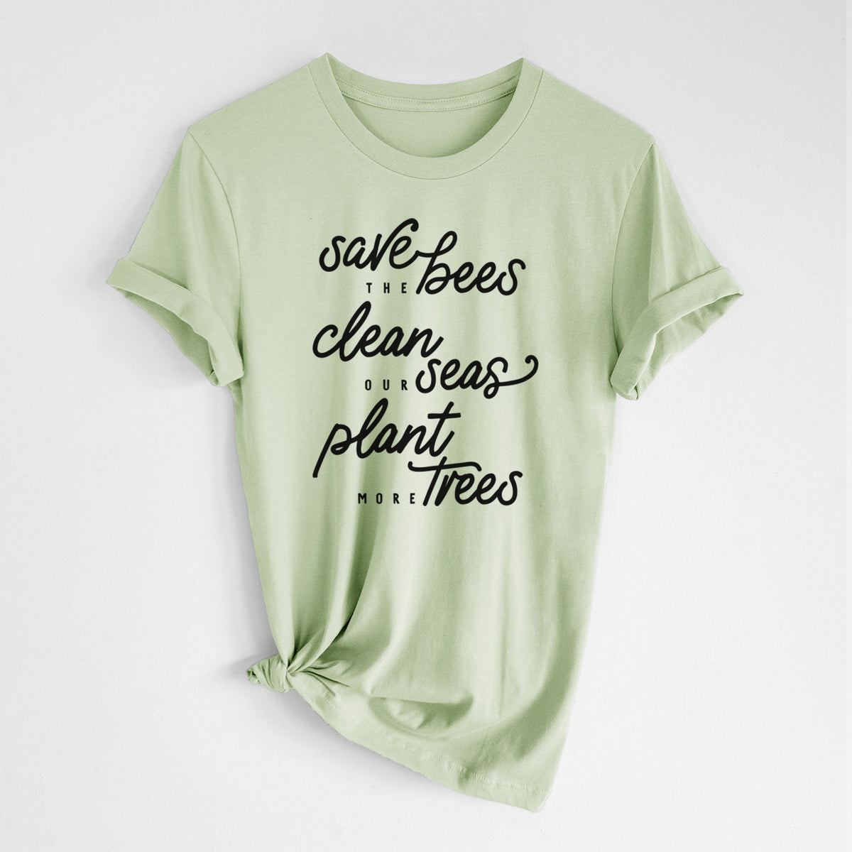 Spring green lightweight cotton t-shirt laid flat with the sleeves rolled, printed with black hand-lettered words reading Save the Bees, Clean Our Seas, Plant More Trees.
