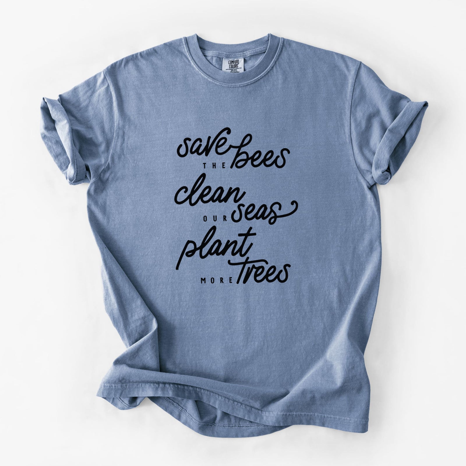 Blue jean Comfort Colors t-shirt laid flat, printed with black hand-lettered words reading Save the Bees, Clean Our Seas, Plant More Trees.