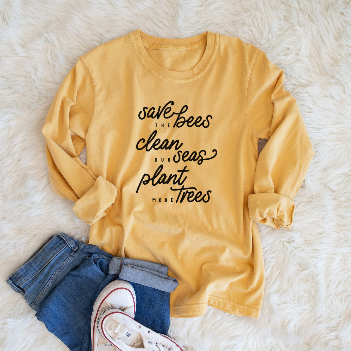 Golden wheat yellow Comfort Colors long sleeve shirt printed with black hand-lettered words reading Save the Bees, Clean Our Seas, Plant More Trees, shown in a lifestyle photo.
