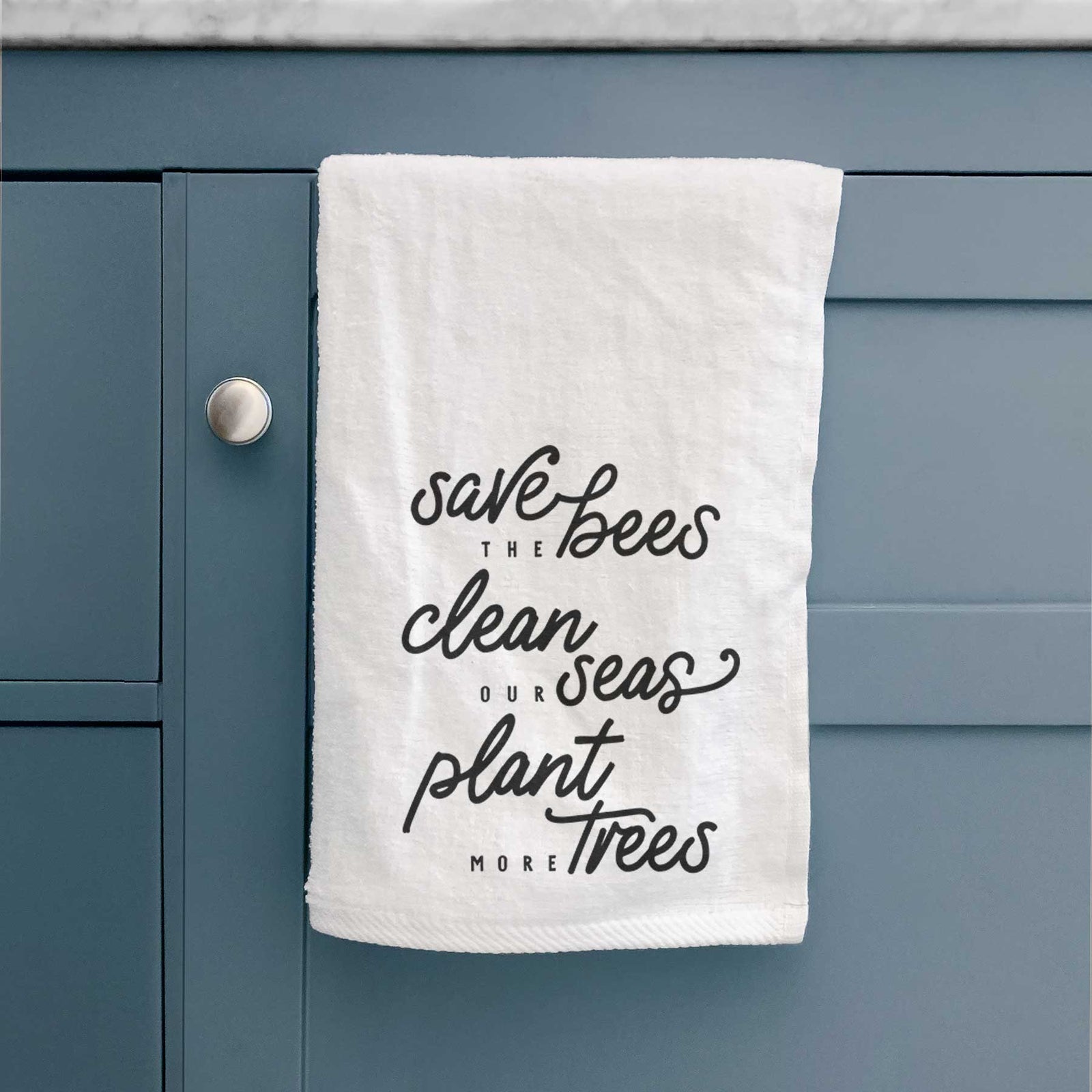 White hand towel printed with black hand-lettered words reading Save the Bees, Clean Our Seas, Plant More Trees.