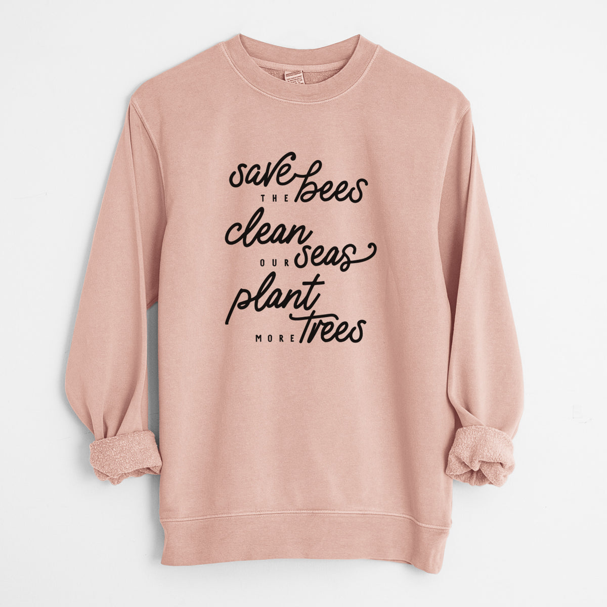 Dusty pink pigment dyed crewneck sweatshirt laid flat with the sleeves rolled, printed with black hand-lettered words reading Save the Bees, Clean Our Seas, Plant More Trees.