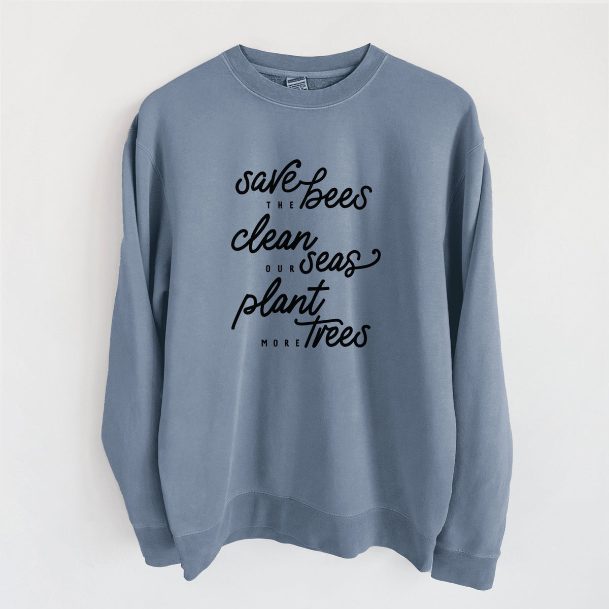 Slate blue pigment dyed crewneck sweatshirt laid flat, printed with black hand-lettered words reading Save the Bees, Clean Our Seas, Plant More Trees.