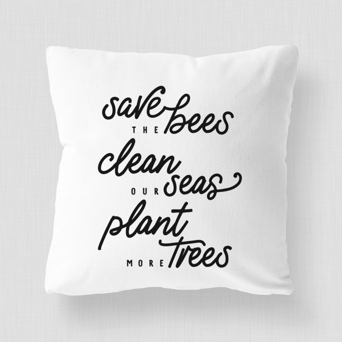 White pillow cover printed with black hand-lettered words reading Save the Bees, Clean Our Seas, Plant More Trees.
