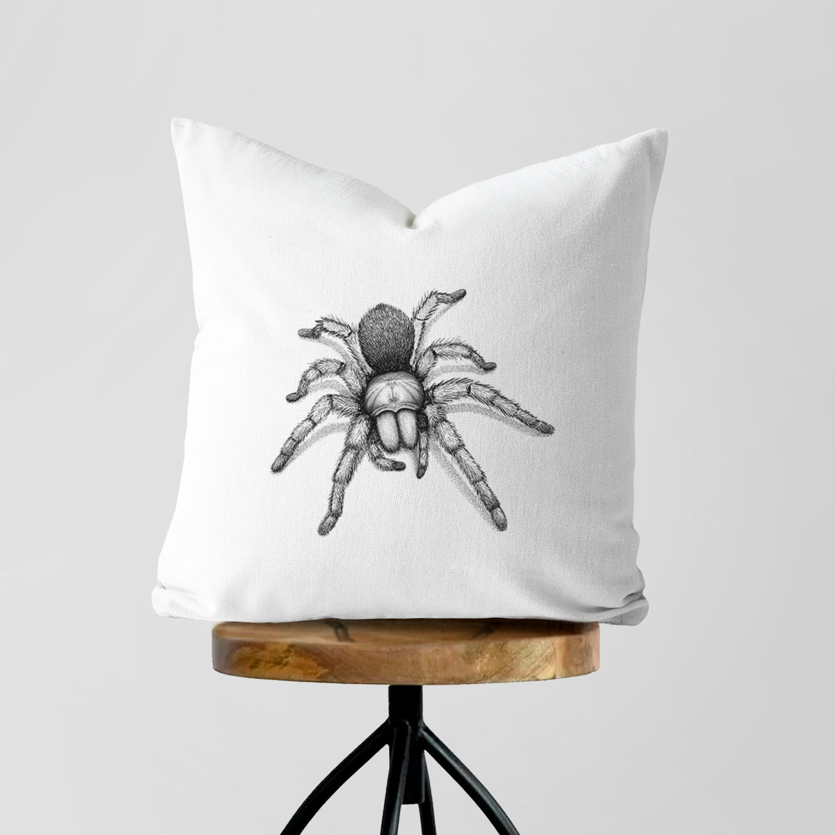 White pillow cover printed with a detailed black ink illustration of a desert blonde tarantula, on a wooden stool.