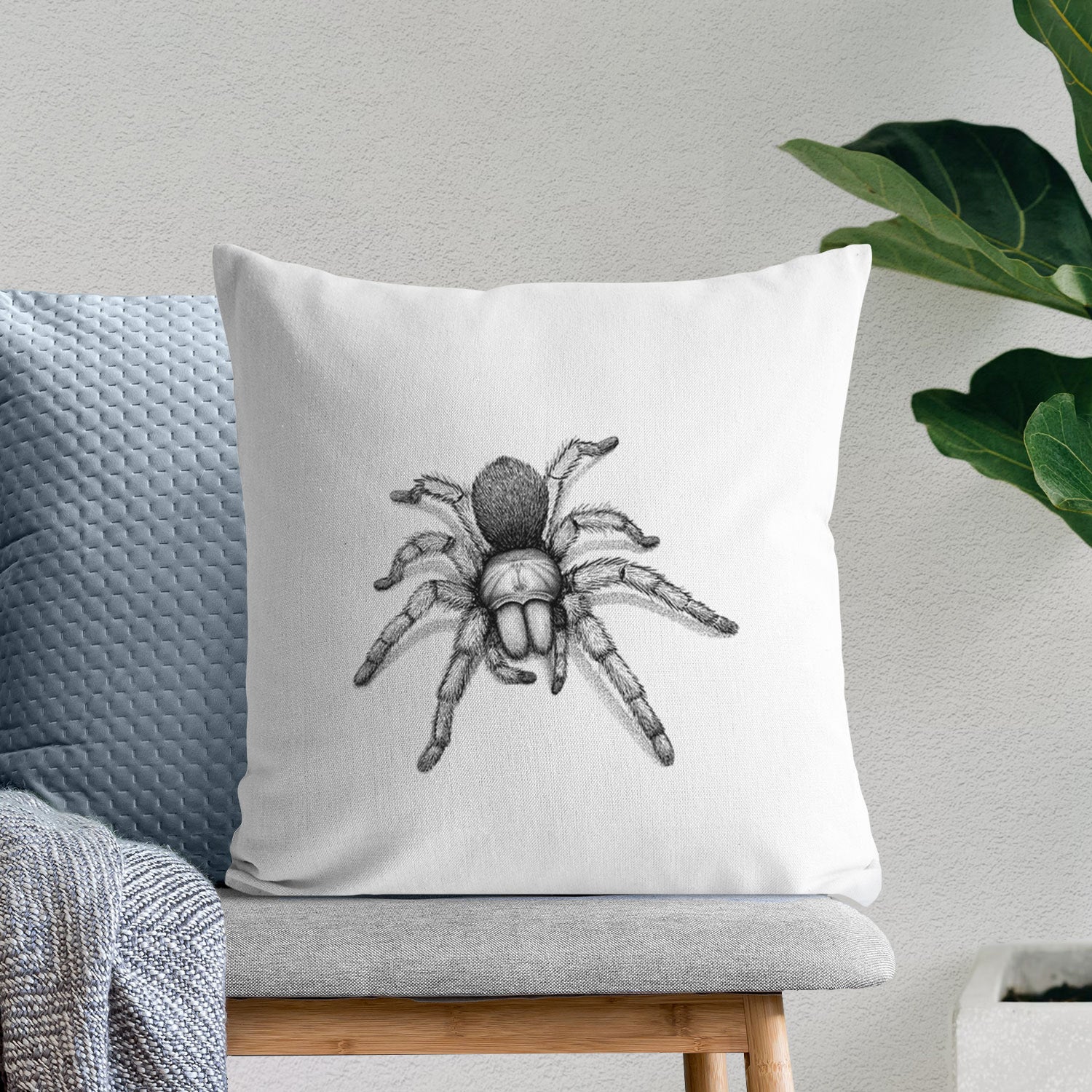 White pillow cover printed with a detailed black ink illustration of a desert blonde tarantula, on a bench beside plants.