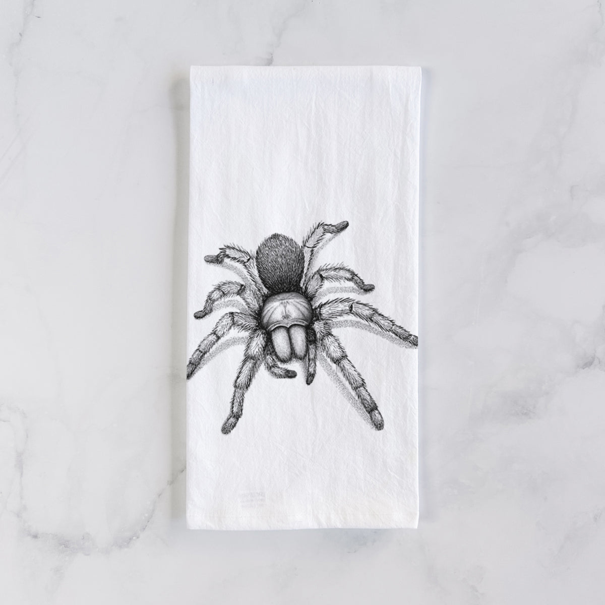 White cotton tea towel laid flat on marble, printed with a detailed black ink illustration of a desert blonde tarantula.