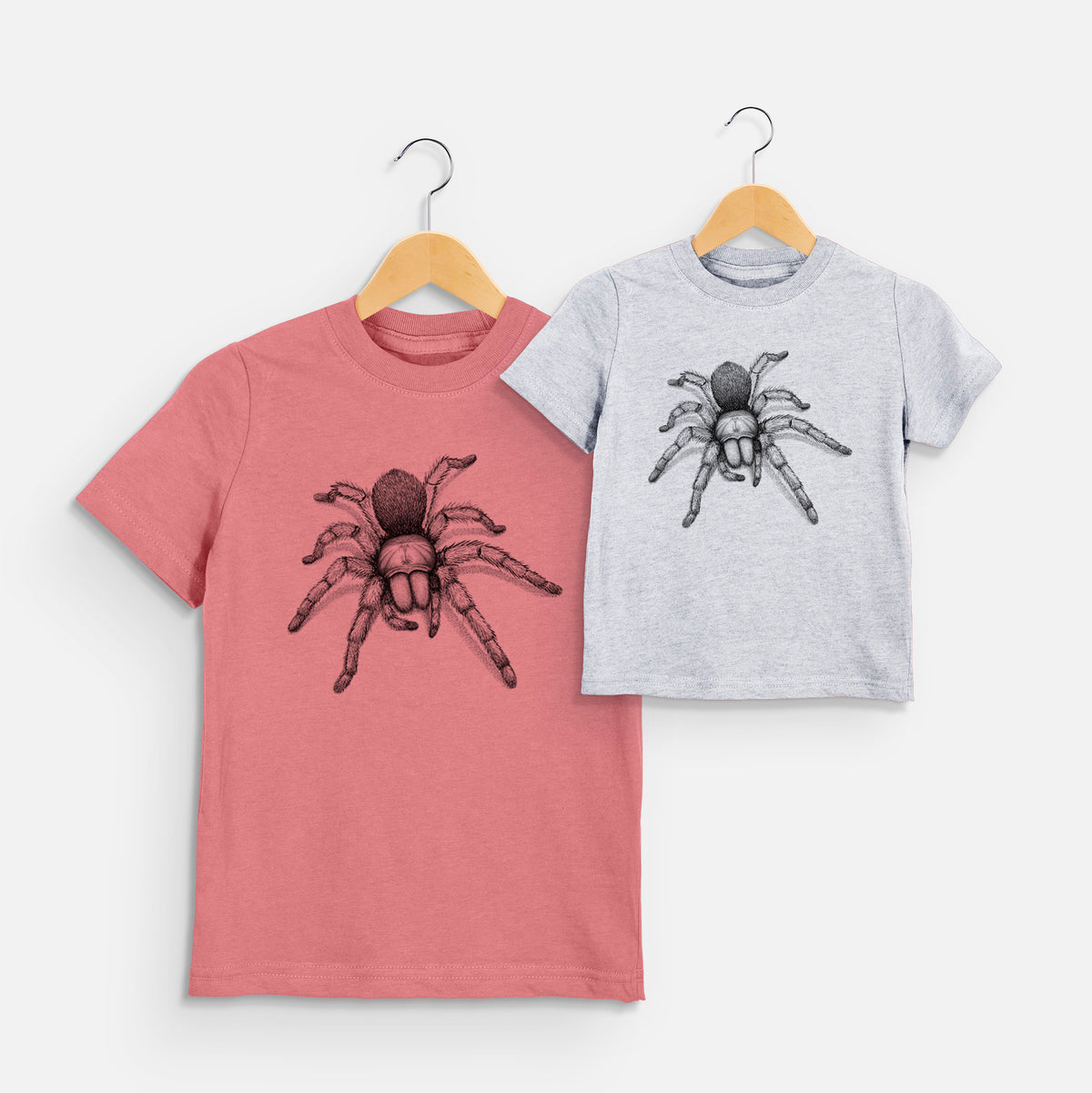 Two youth t-shirts in different colors on hangers, printed with a detailed black ink illustration of a desert blonde tarantula.