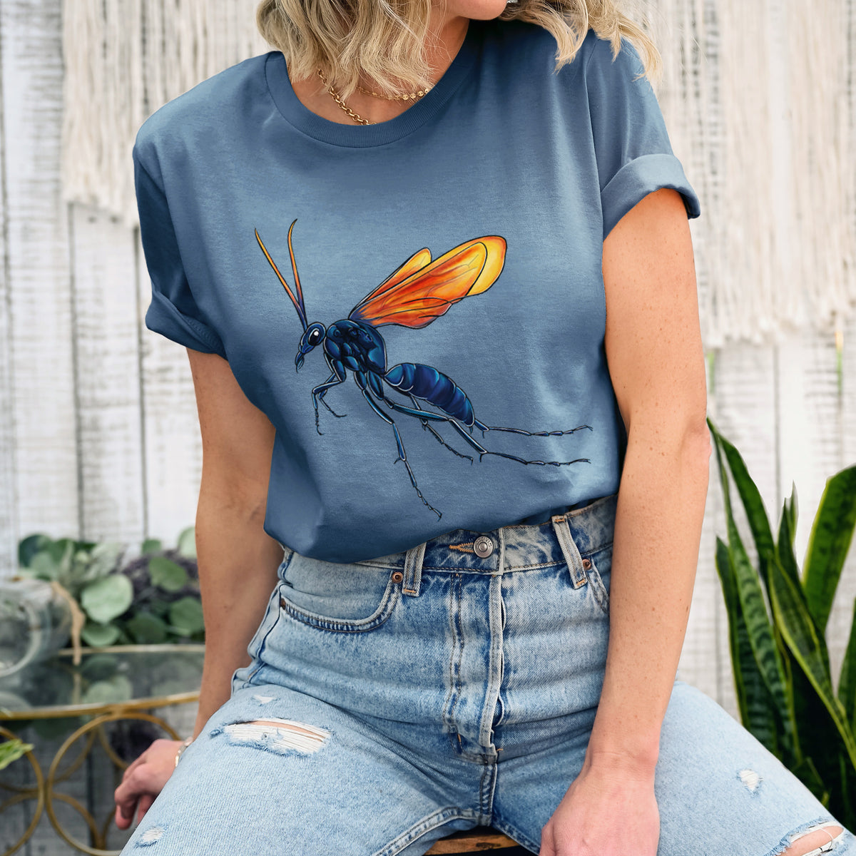 Woman wearing a steel blue lightweight cotton t-shirt printed with a full-color illustration of a tarantula hawk wasp with a blue body and orange wings.