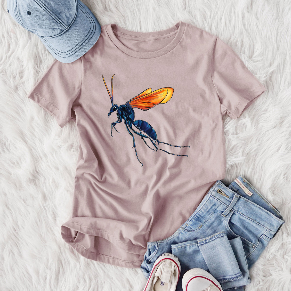 Women's relaxed fit cotton t-shirt printed with a full-color illustration of a tarantula hawk wasp with a blue body and orange wings, styled flat on a white faux fur rug with jeans.