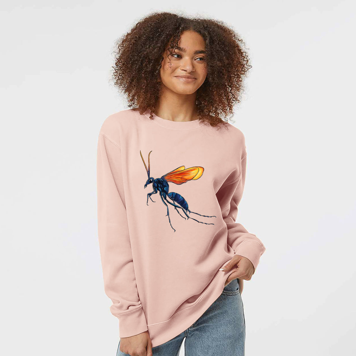 Model wearing a dusty pink pigment dyed crewneck sweatshirt printed with a full-color illustration of a tarantula hawk wasp with a blue body and orange wings.