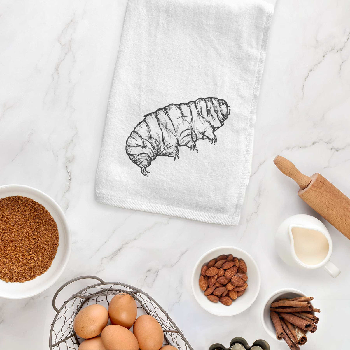 White hand towel printed with a detailed black ink illustration of a tardigrade, or water bear, hanging on a cabinet door.